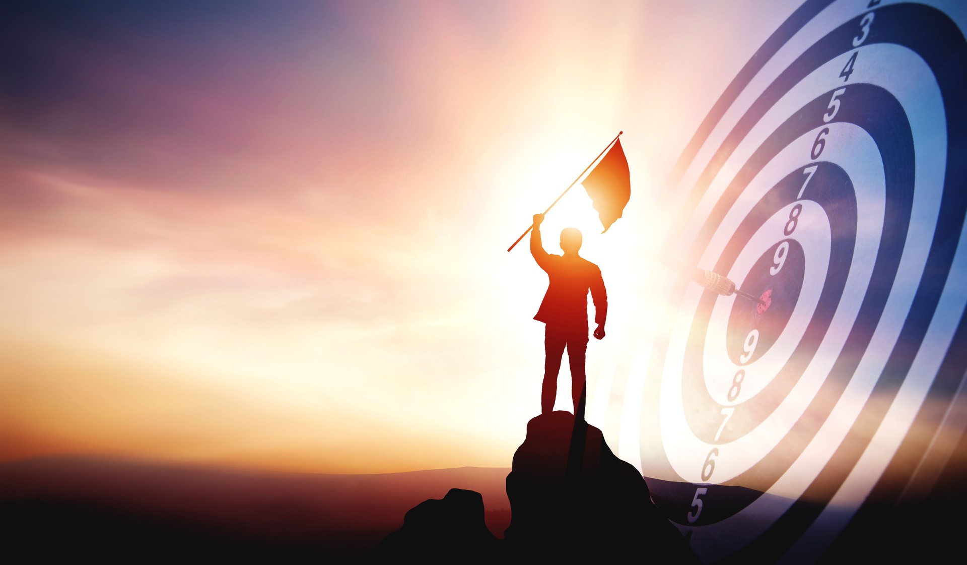 Silhouette of businessman holding a flag on top mountain with a target board showing victory.